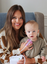Woman holding a baby and a device, sitting on a couch.